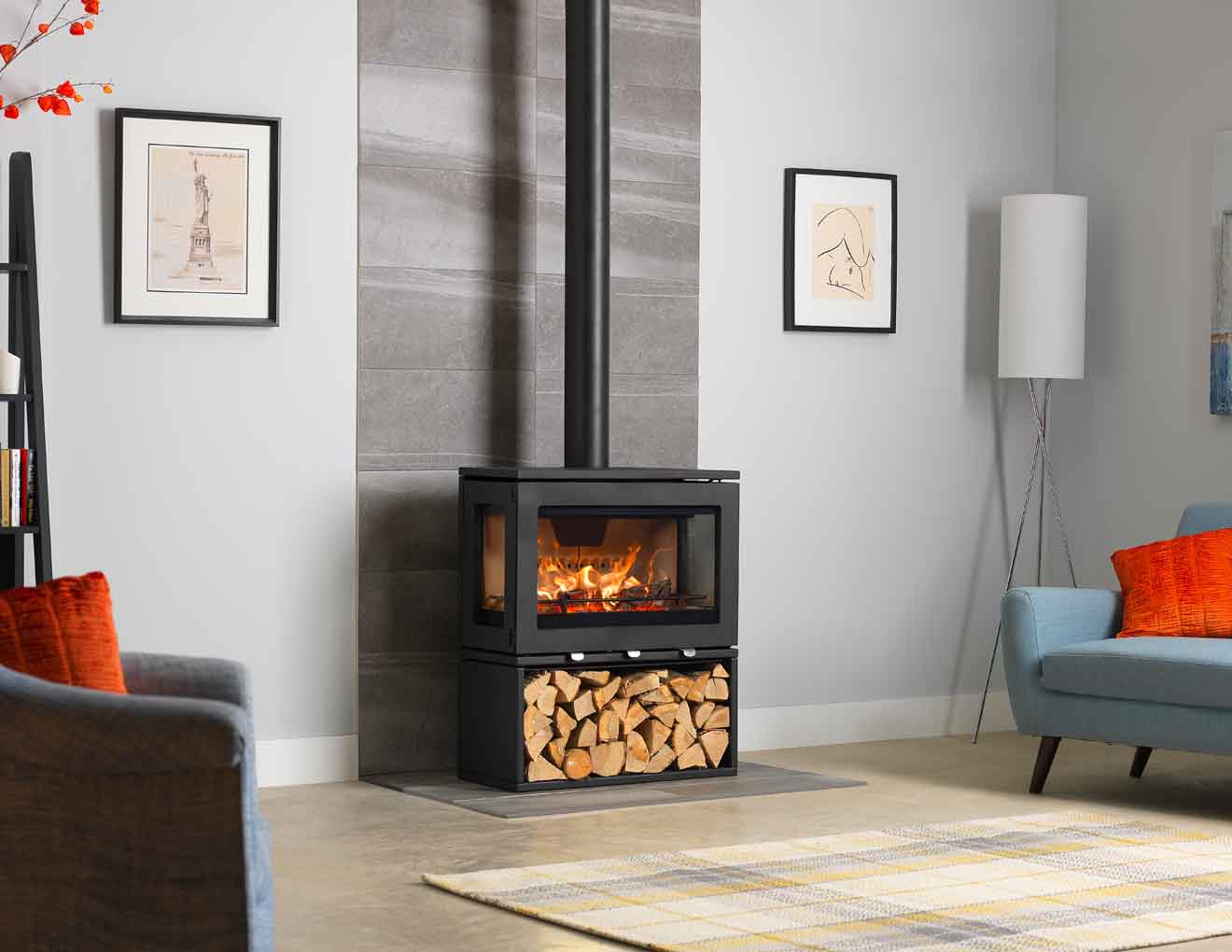 Charlton & Jenrick PureVision LPV8 black wood-burning stove with three-sided panoramic glass, glowing flames and dedicated log store in a modern living room, Cork, Homexpert